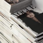 Design Trends - High angle many fashion magazines stacked on floor against white brick wall in studio